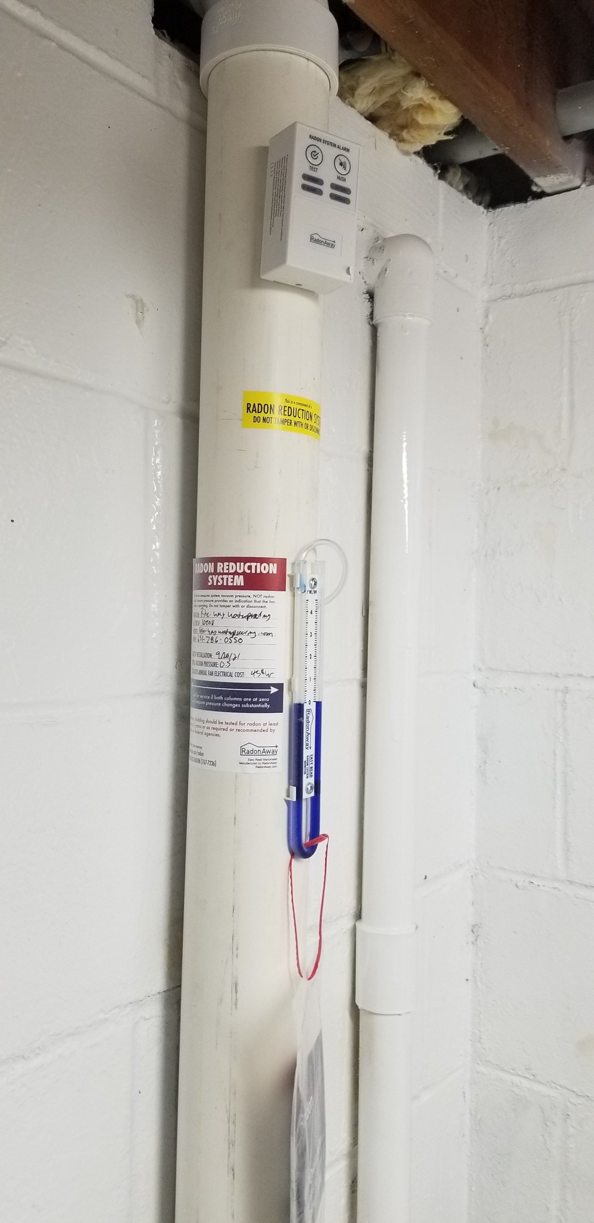 White water heater tank with labels and blue thermometer in a basement corner