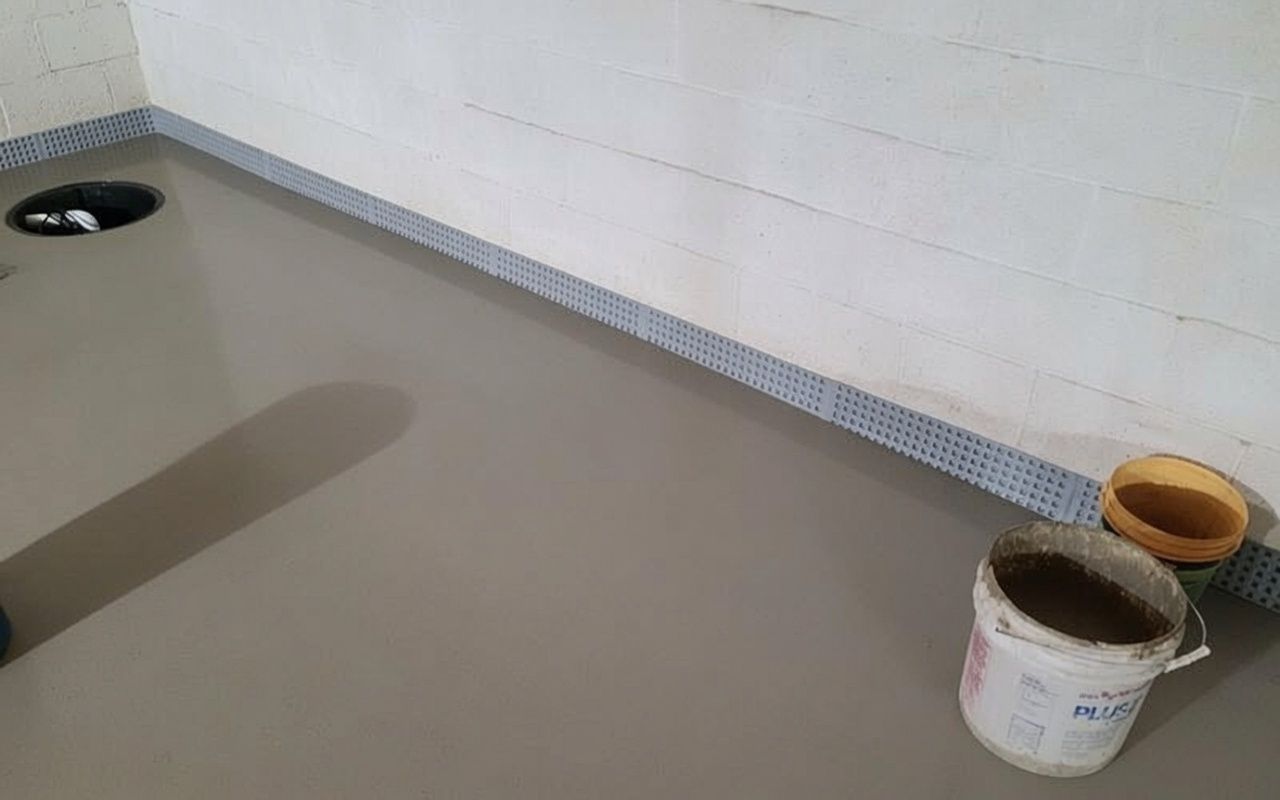 Indoor room corner with newly poured gray concrete floor and paint buckets against a white wall.
