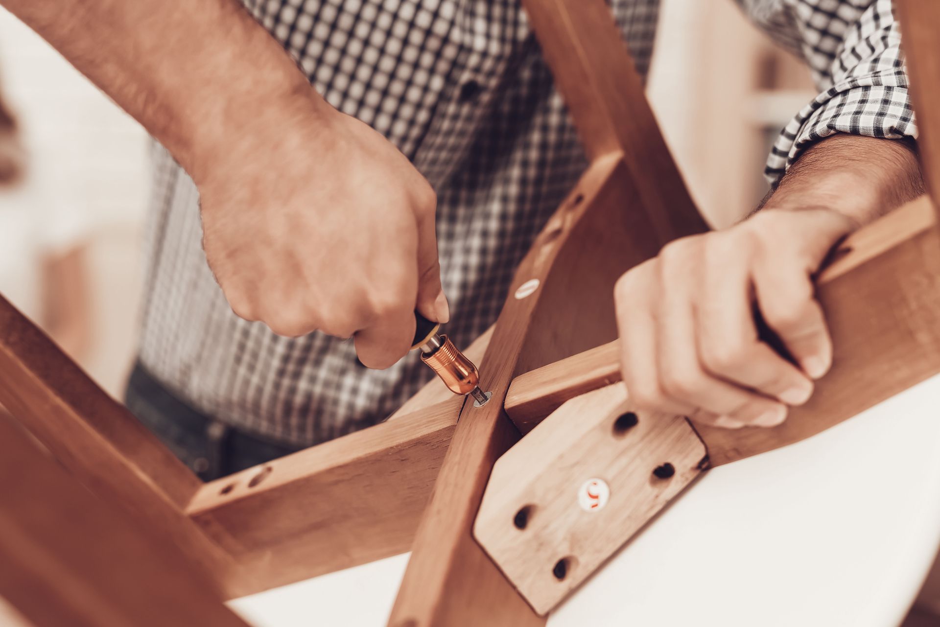 Person assembling wooden chair with a screwdriver indoors.