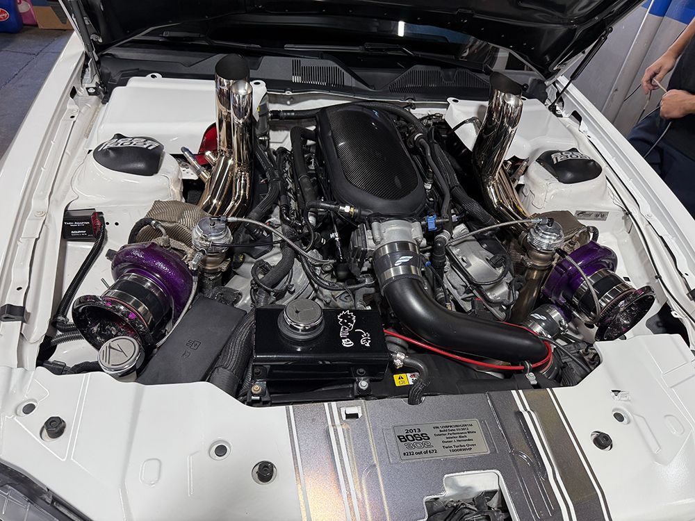 White car engine bay with purple turbochargers and chrome exhaust manifolds.