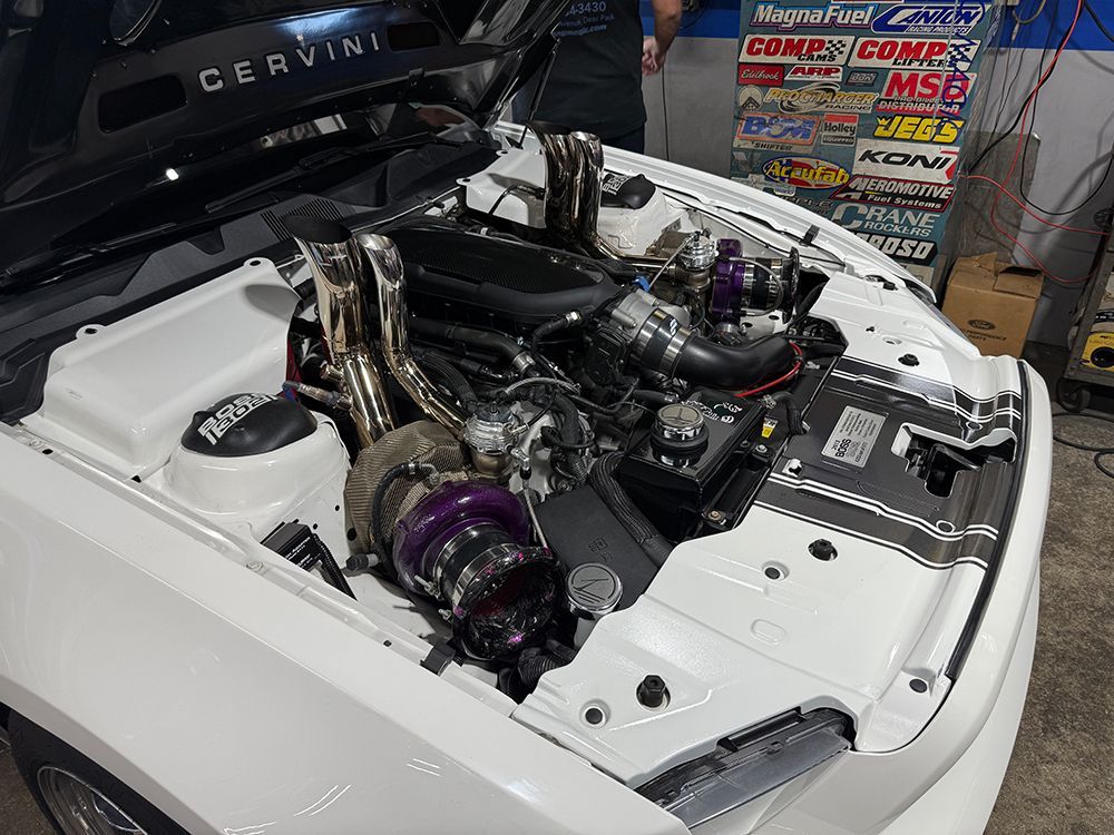 White car engine bay, customized with turbochargers, headers, and performance parts.