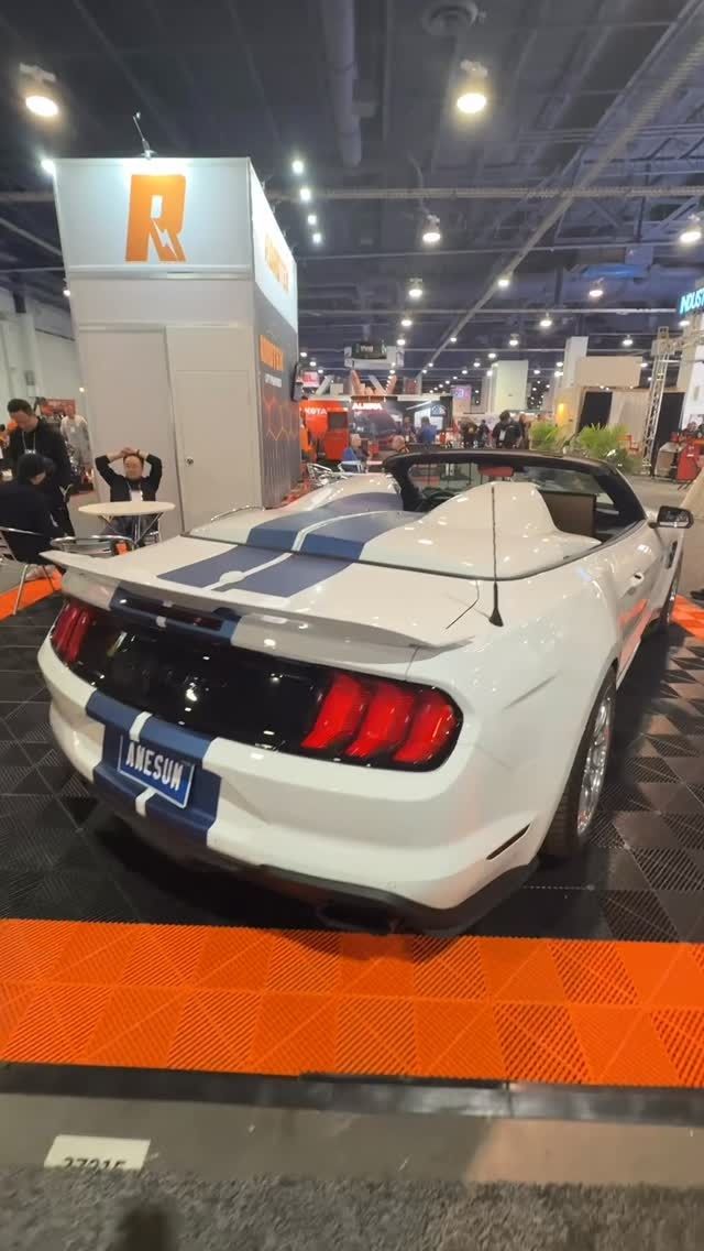 White Ford Mustang convertible with blue racing stripes; at a trade show.