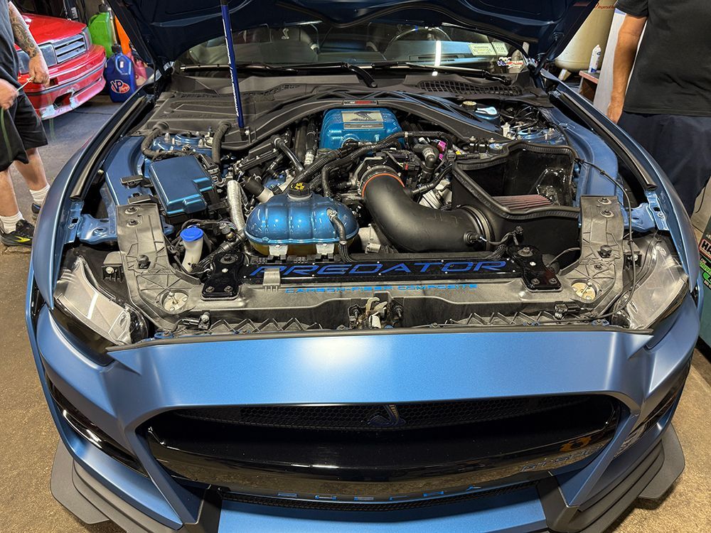 Blue Ford Mustang with the hood up, showing a modified engine.