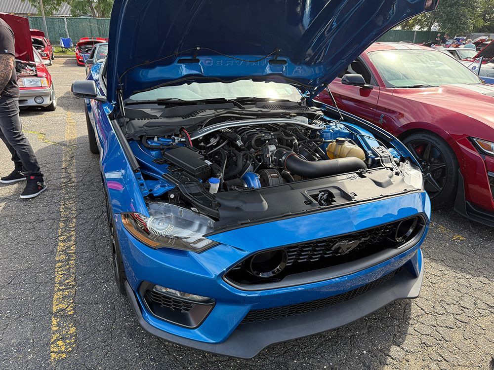Blue Ford Mustang with hood open, parked at a car show.