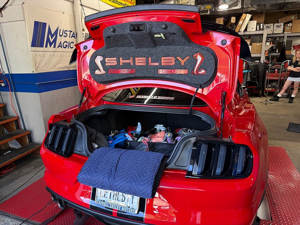 Red Shelby Mustang with trunk open, in a garage. 