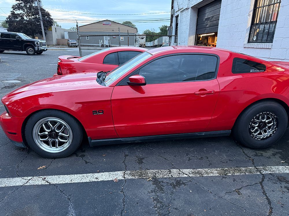 Red Ford Mustang parked outside a building with another car in the background.