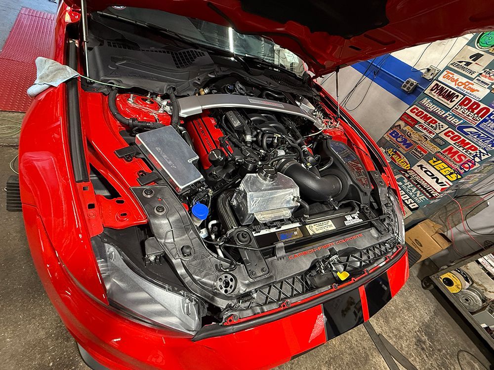 Red Mustang with open hood, engine bay visible in a shop.