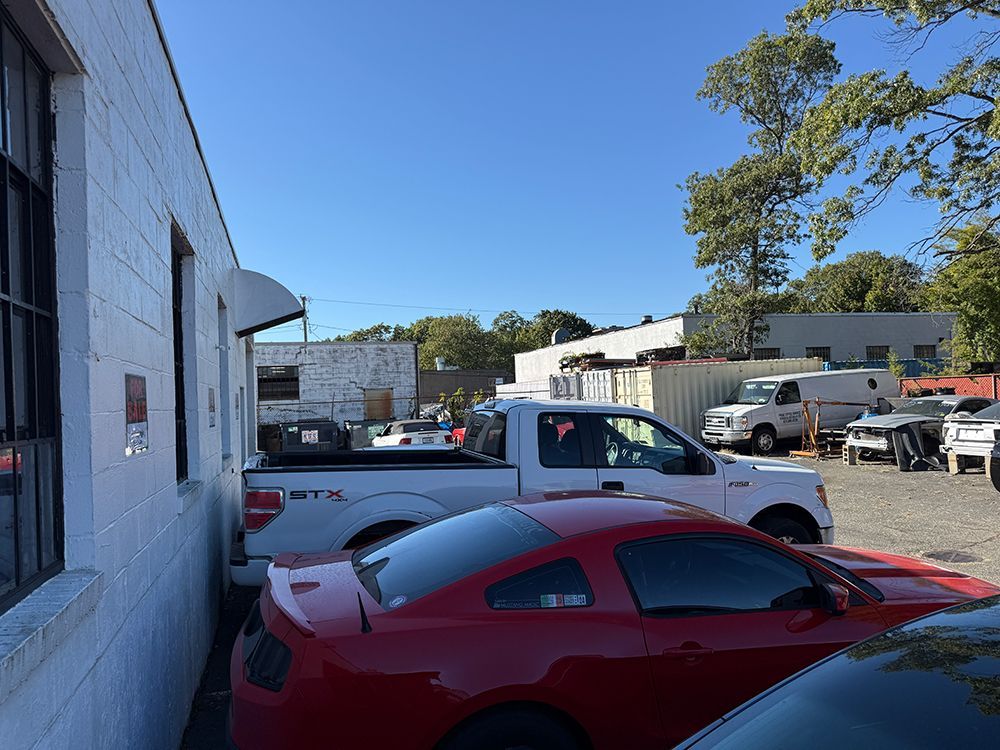 White building next to a parking lot with various cars and trucks under a blue sky.