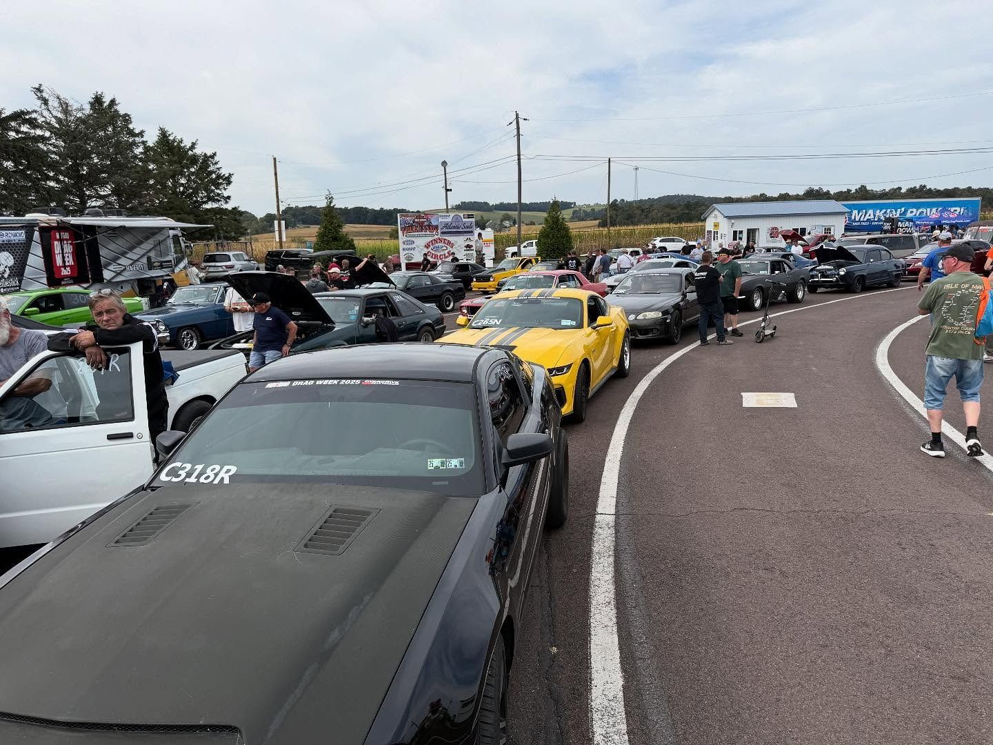 Cars lined up at a car show, including a yellow Mustang. People are around the cars outdoors.