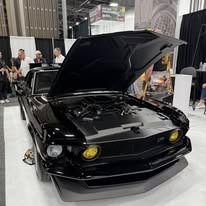 Black classic car with hood up at an auto show. Yellow headlights.