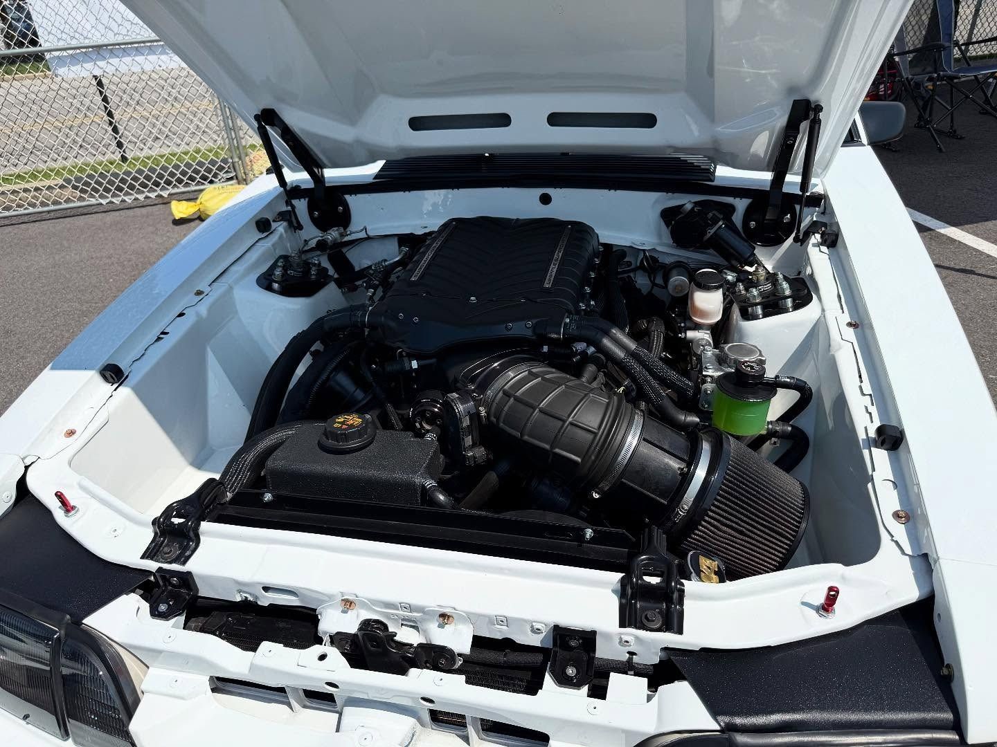 White car engine compartment, black engine, open hood, visible air intake, green fluid.