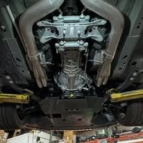 Undercarriage of a vehicle showing exhaust pipes, transmission, and suspension components.