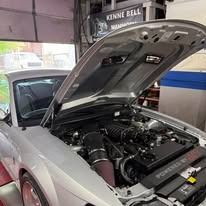 Silver car with hood open, engine details visible, in a workshop.