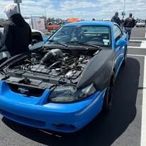 Blue sports car with a modified engine bay. Outdoors, sunny.