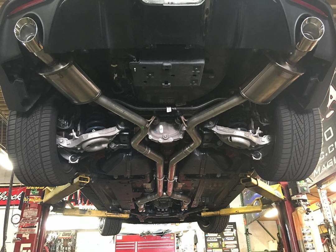 Underneath view of a car on a lift, showing its exhaust system with two chrome pipes. Black car, gray exhaust.