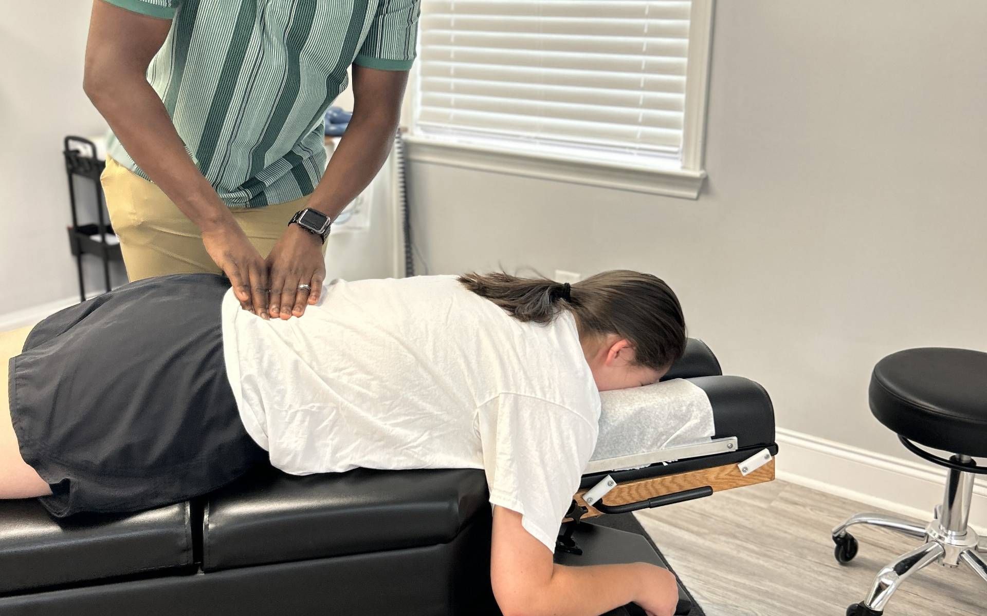 Chiropractor adjusting patient's back in a clinic. Man in green shirt, woman in white shirt lying face down.