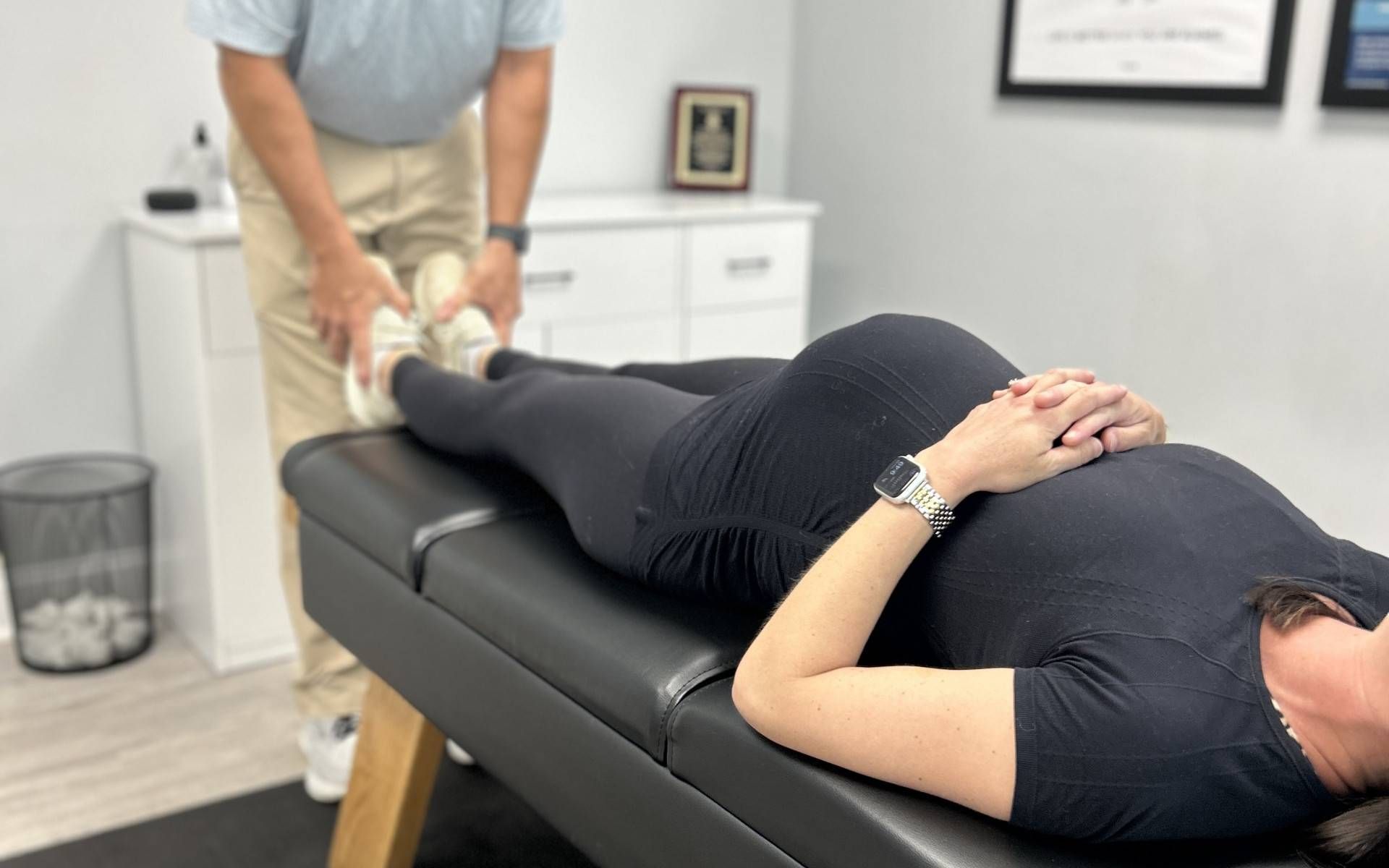 Chiropractor adjusting pregnant woman's legs on examination table; neutral setting.