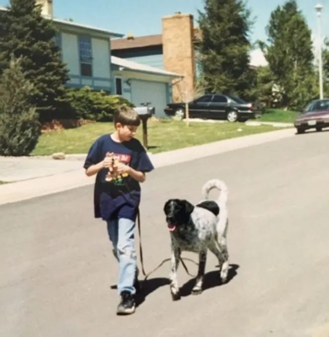 A boy is walking a dog on a leash in front of a house