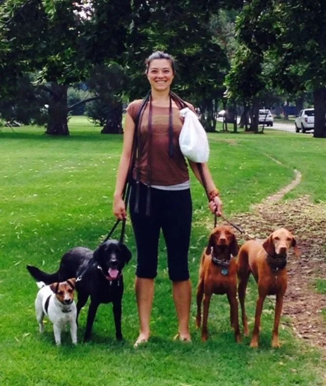 A woman is standing with three dogs in a park