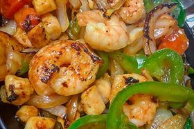 A close up of a plate of food with shrimp , peppers , onions and tomatoes