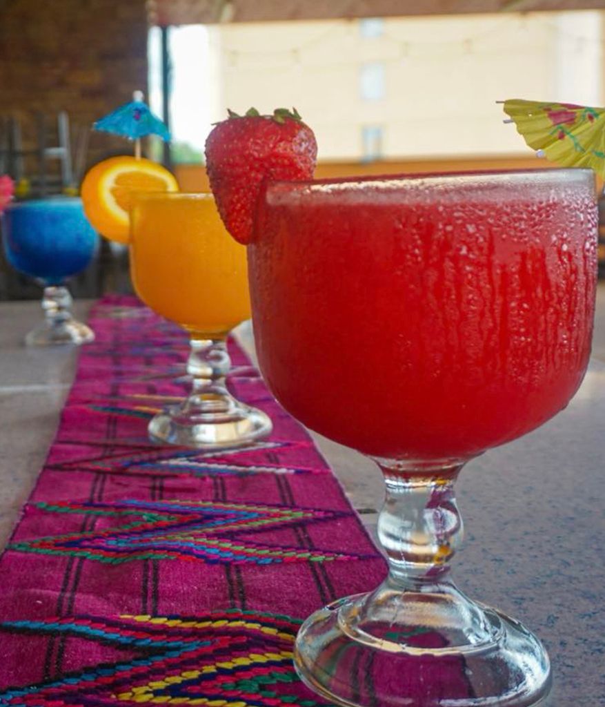 A row of colorful drinks in wine glasses on a table