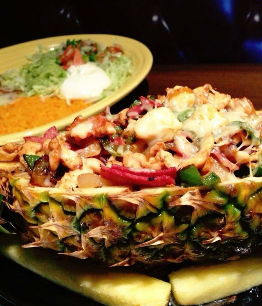 A pineapple filled with food next to a plate of food