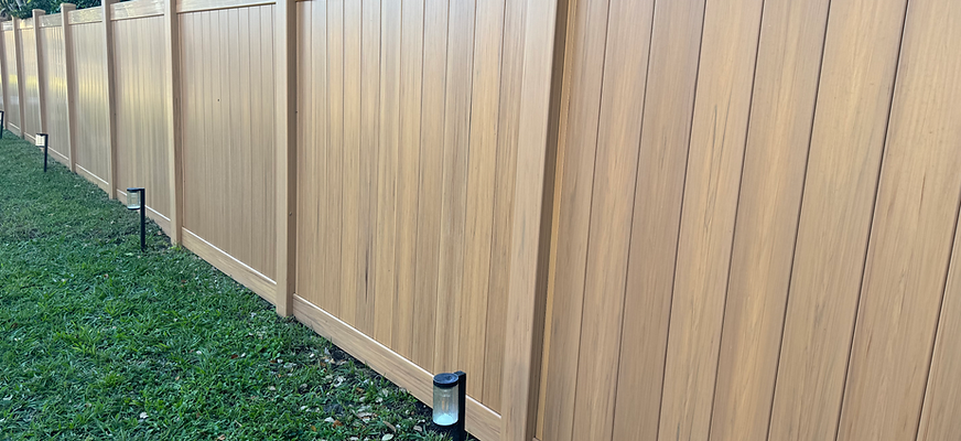 A long, wooden fence in a yard with green grass. Ground lighting is installed along the fence.