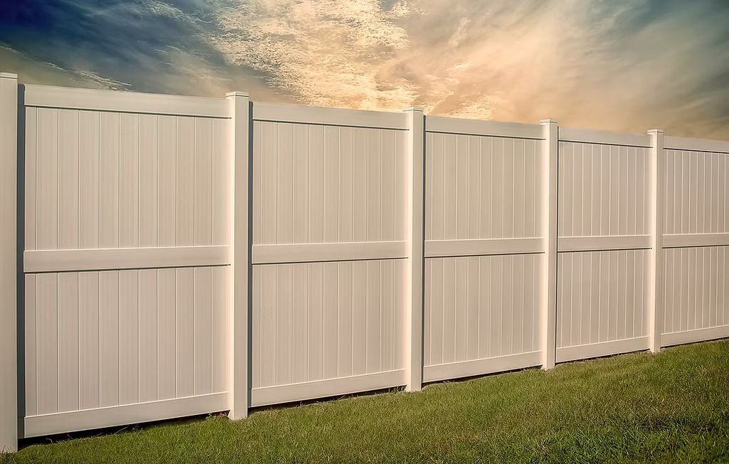 White vinyl privacy fence against a cloudy sky, on a grassy lawn.