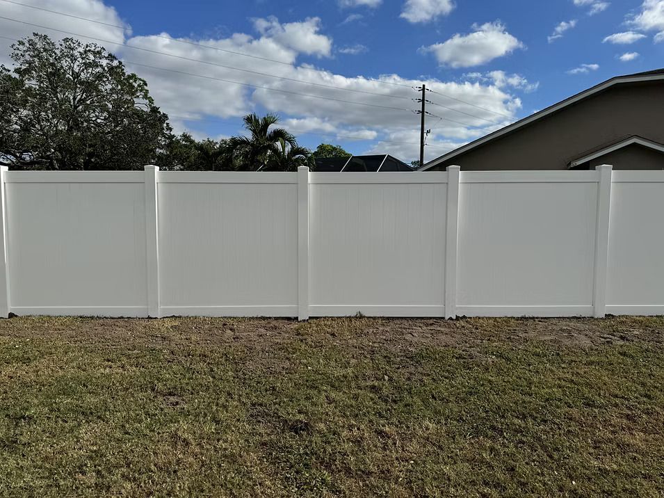 White vinyl fence in front of a grassy yard, with a blue sky and clouds in the background.