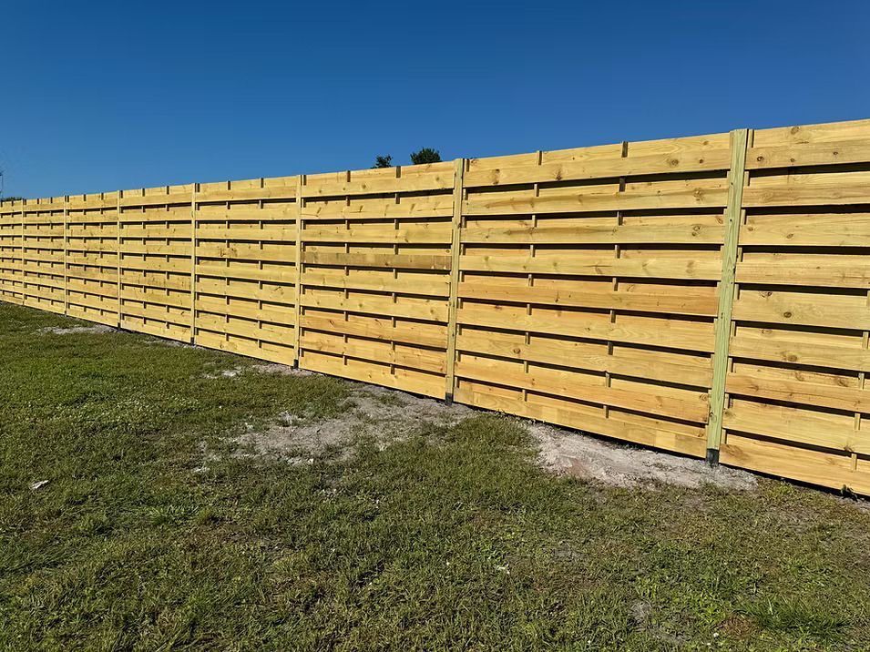 Wooden horizontal slat fence in a grassy field under a blue sky.