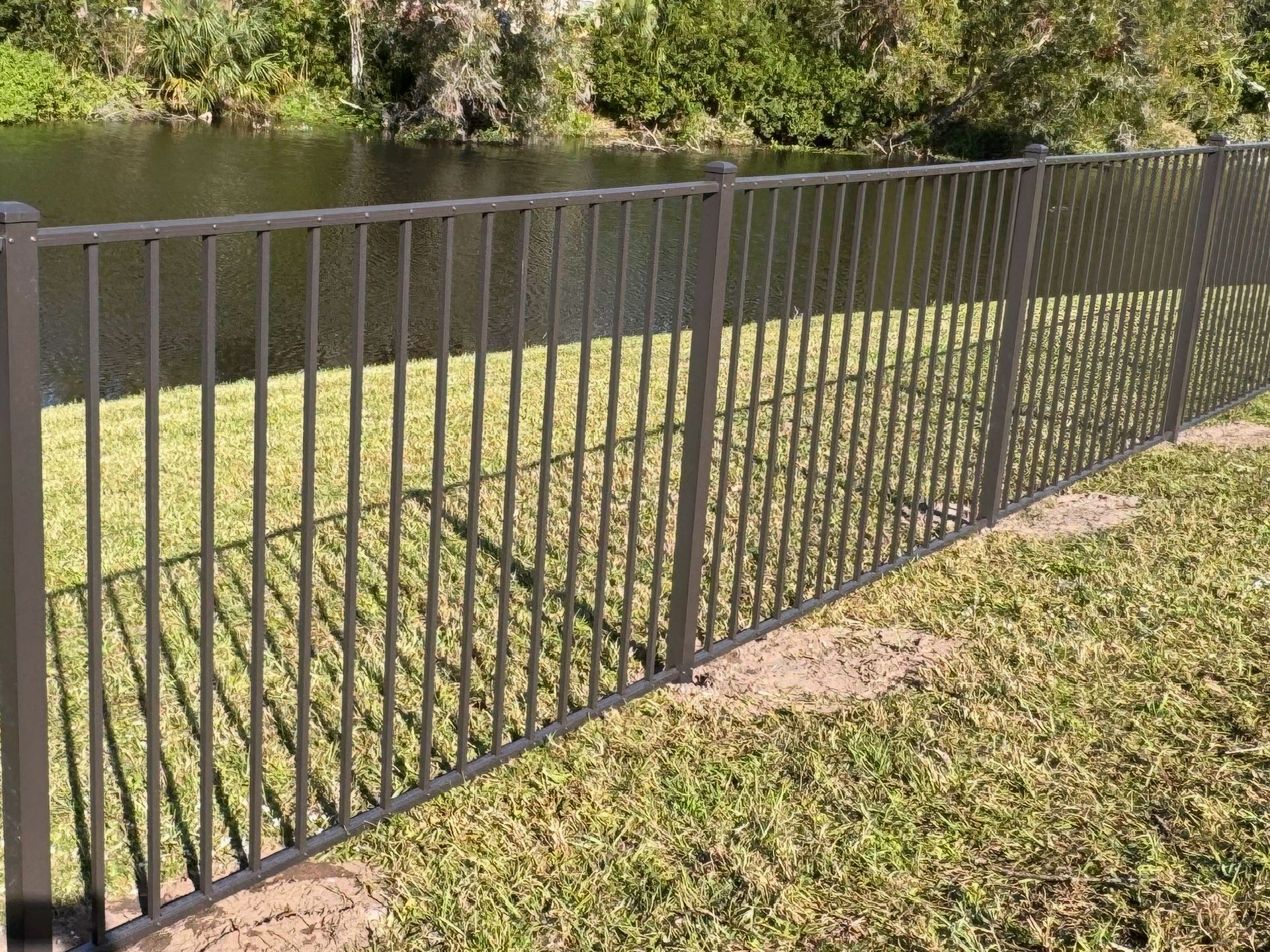 A dark gray metal fence along a grassy yard, next to a body of water.