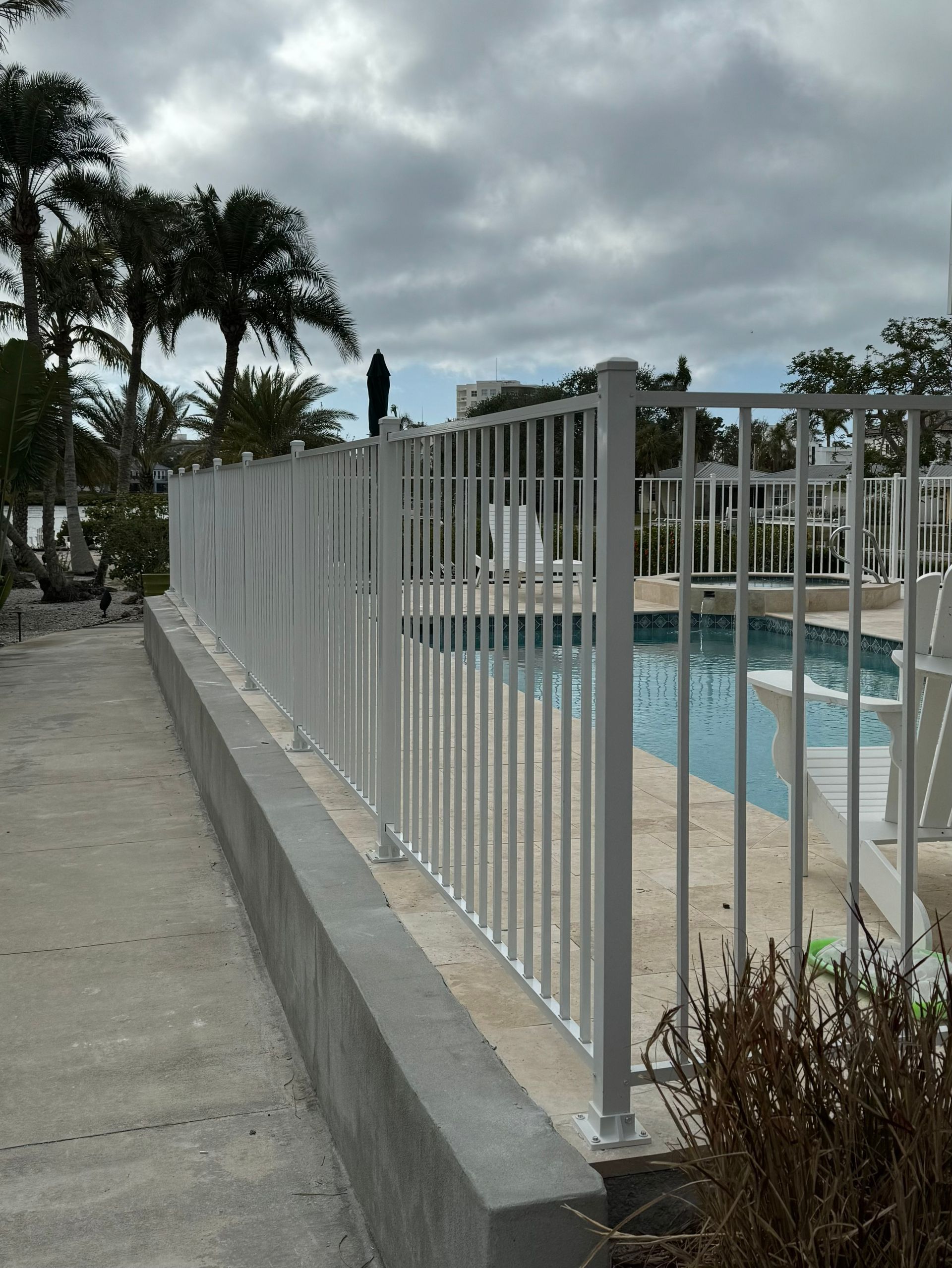 A white metal fence surrounds a pool on a cloudy day.