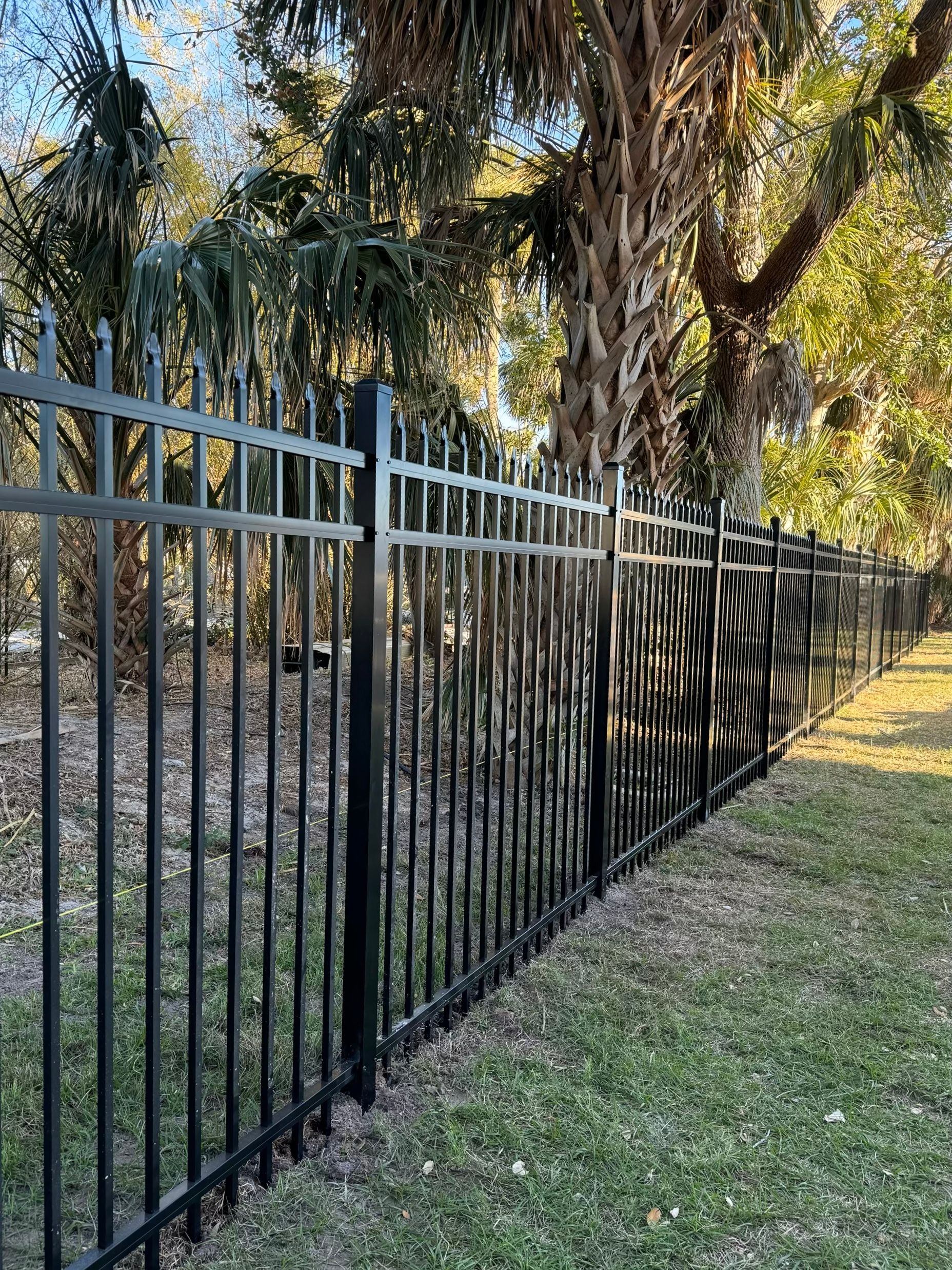 Black metal fence in a yard with grass and trees in the background.