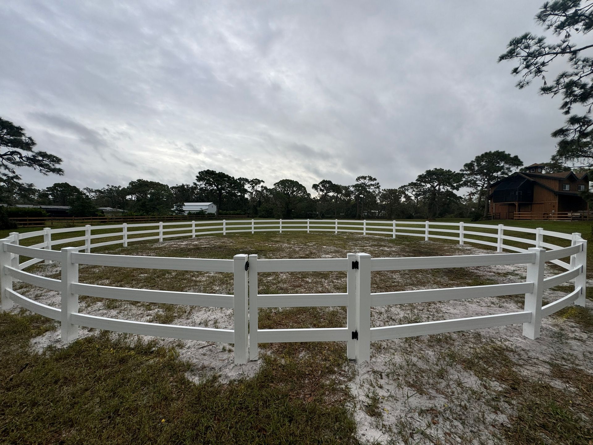 A white circular horse training pen in a grassy field under a cloudy sky.