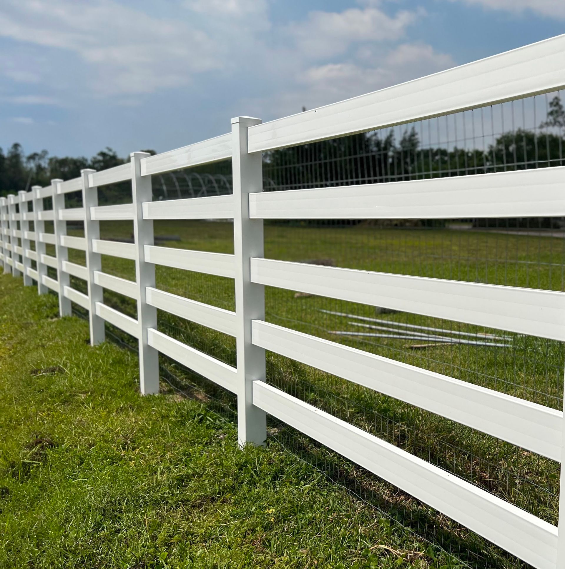 A white fence in a grassy field, under a partly cloudy blue sky.
