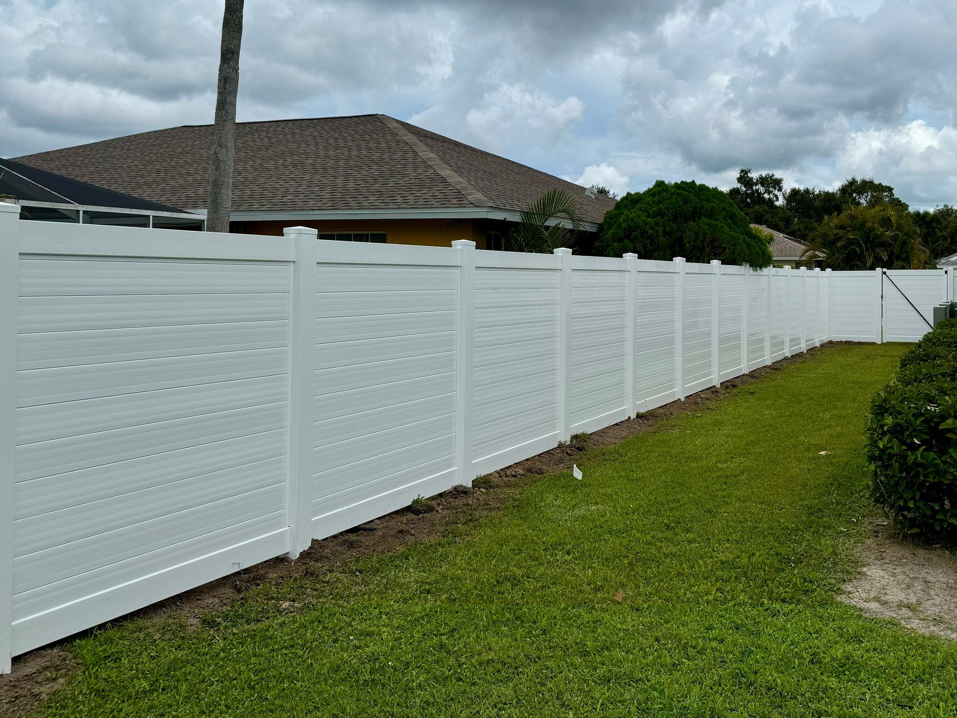 White vinyl fence in a grassy yard, under a cloudy sky.