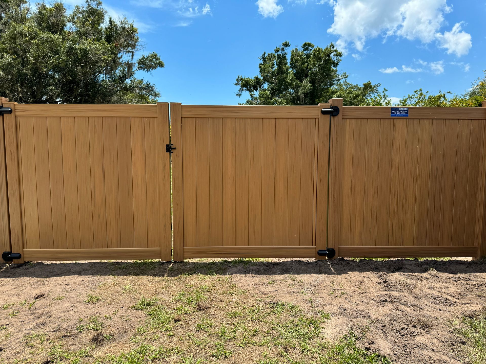 Tan vinyl fence with two gates, under a blue sky.