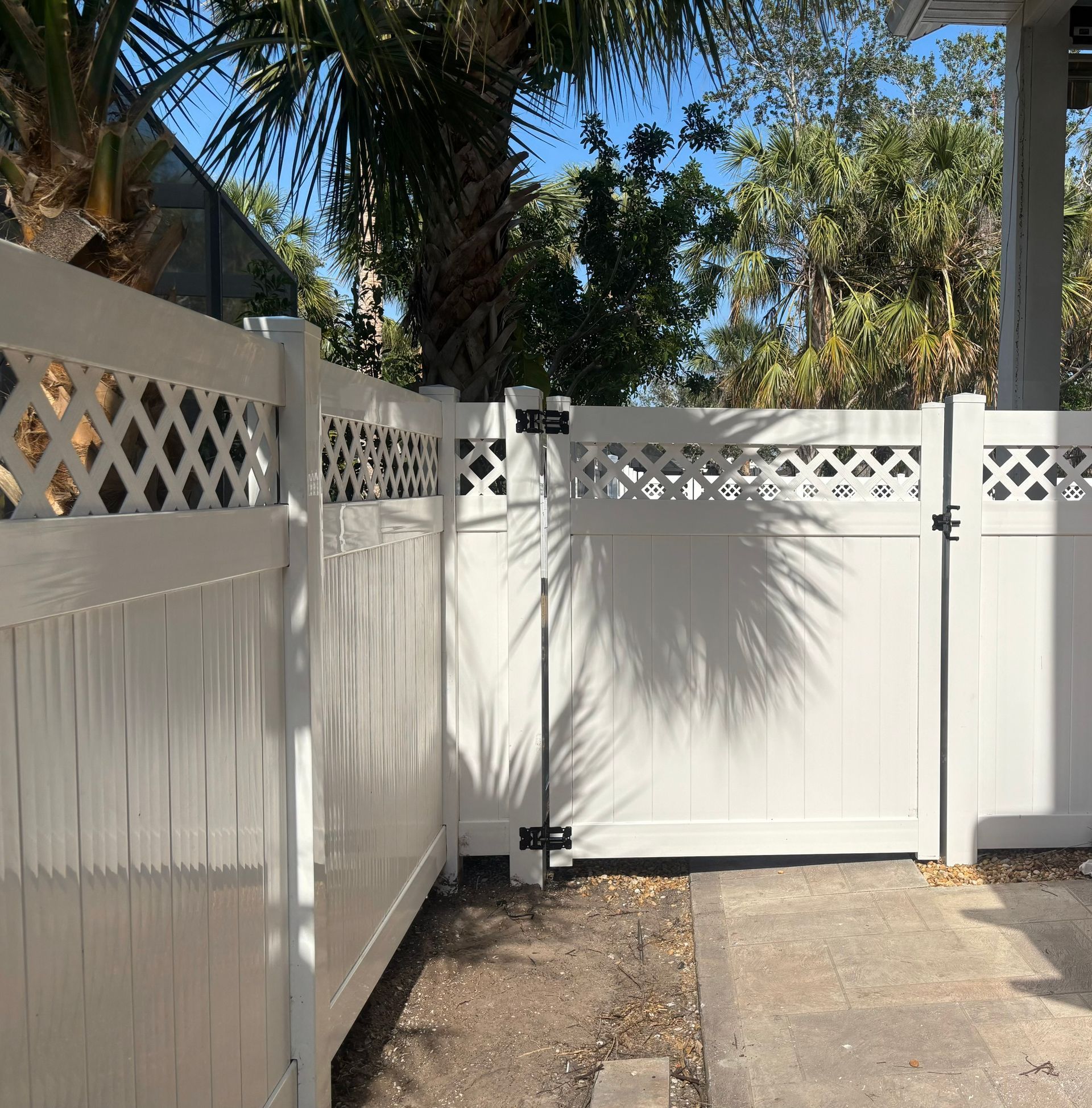 White picket fence with gate in front of palm trees.