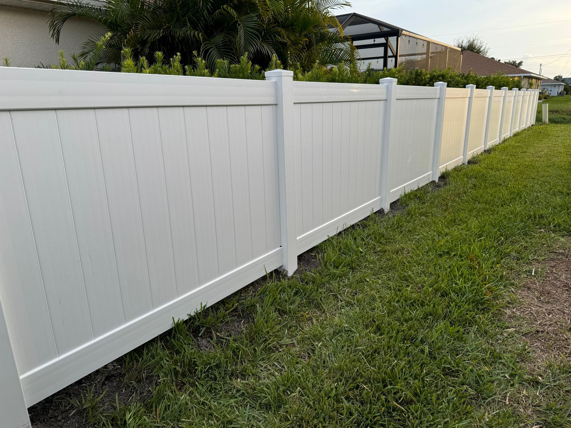 A white vinyl fence borders a grassy yard under a partly cloudy sky.