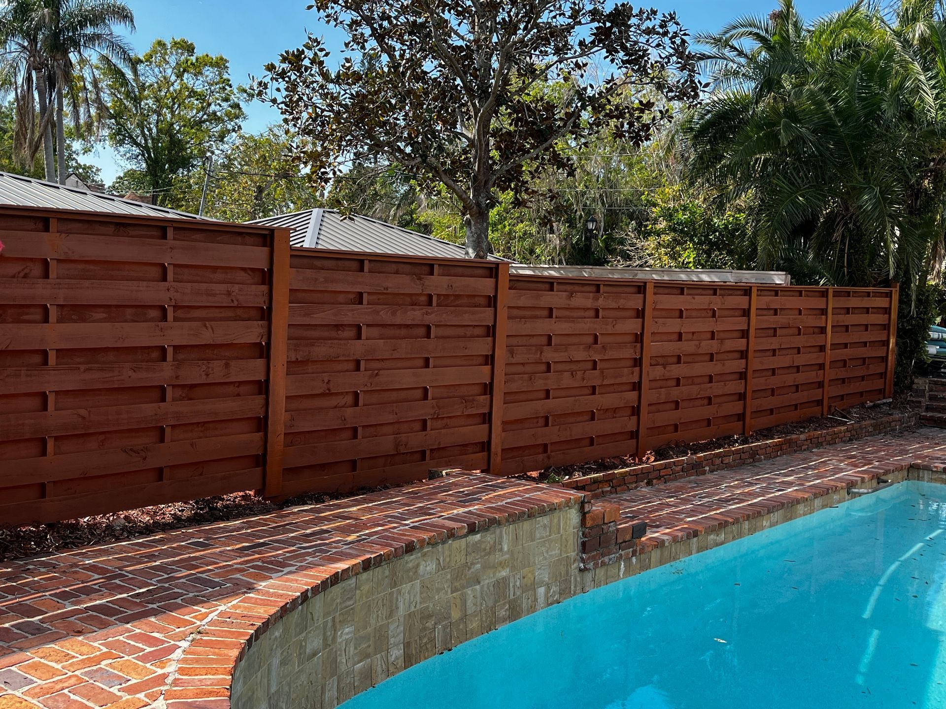 A brown-stained wooden fence alongside a brick-lined pool.
