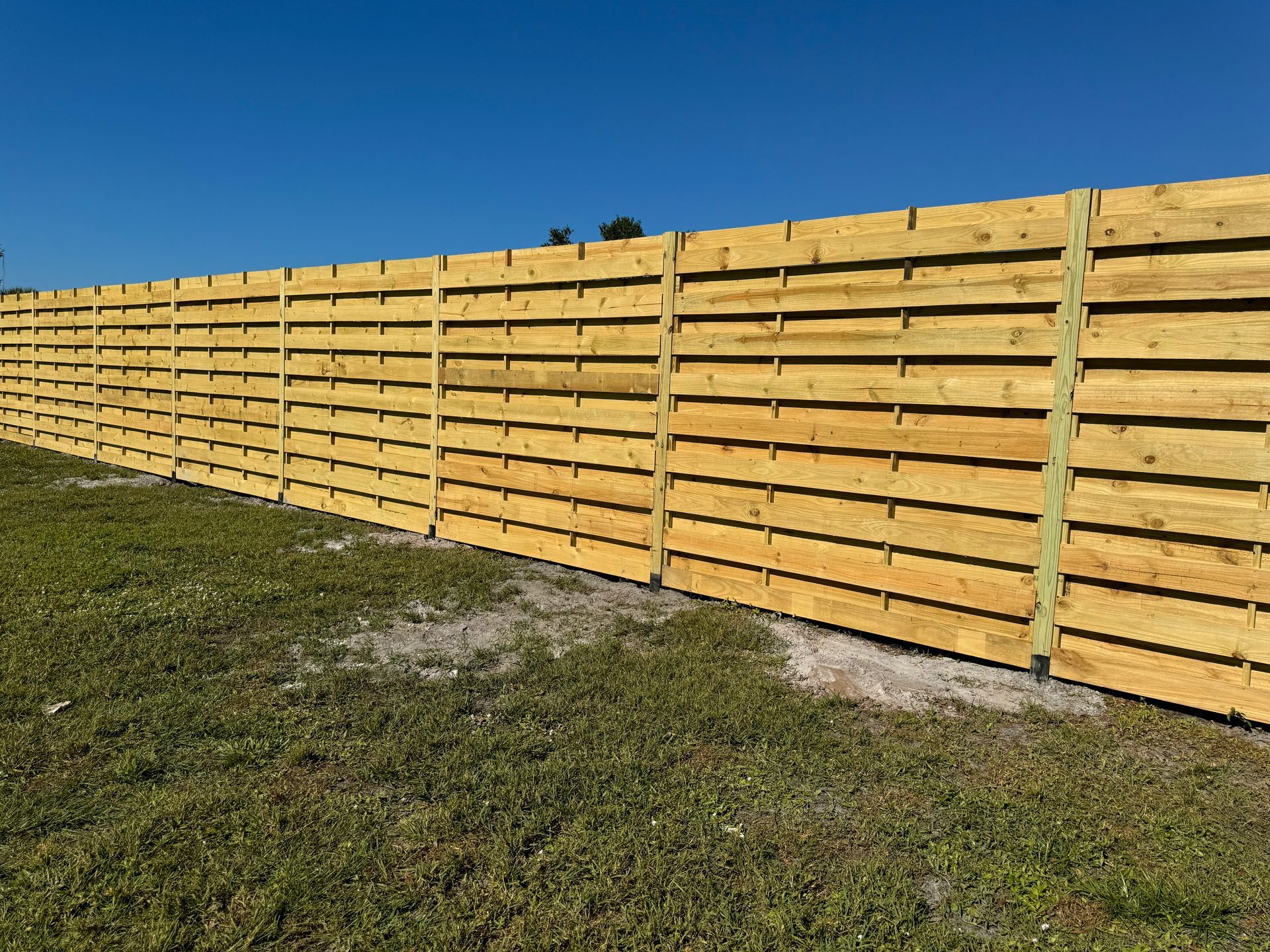 Wooden horizontal slat fence in a grassy yard under a blue sky.