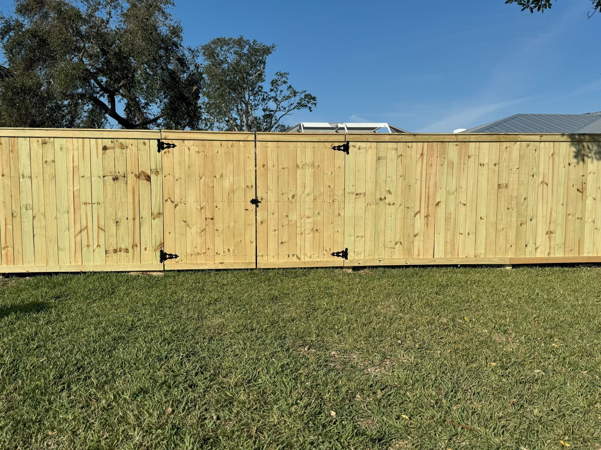 Wooden fence with two gate sections in a grassy yard under a blue sky.