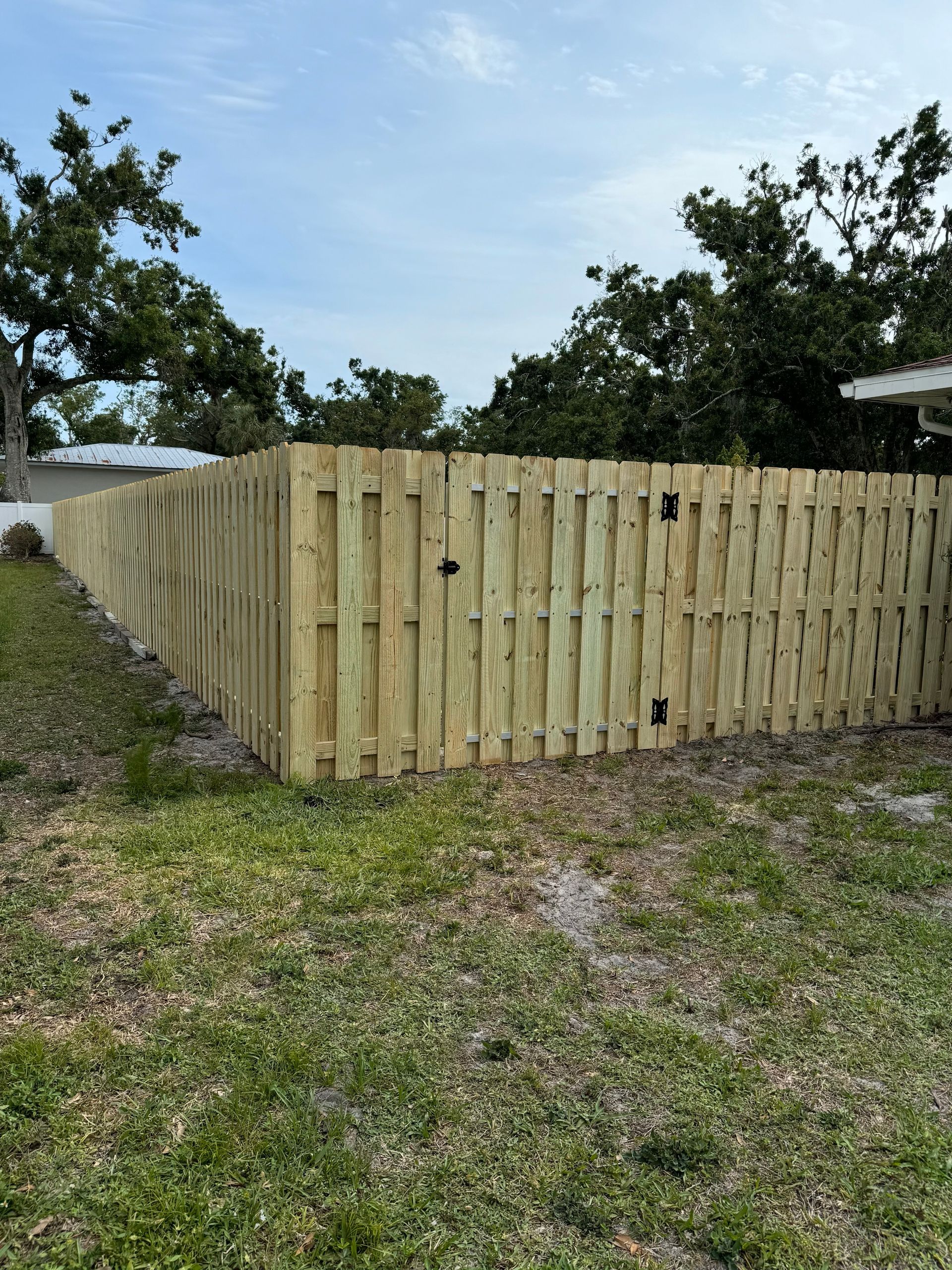 A wooden fence surrounds a grassy yard under a cloudy sky.