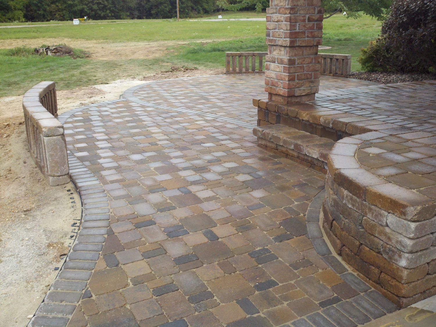 A brick walkway leading to a patio with a stone wall and steps.