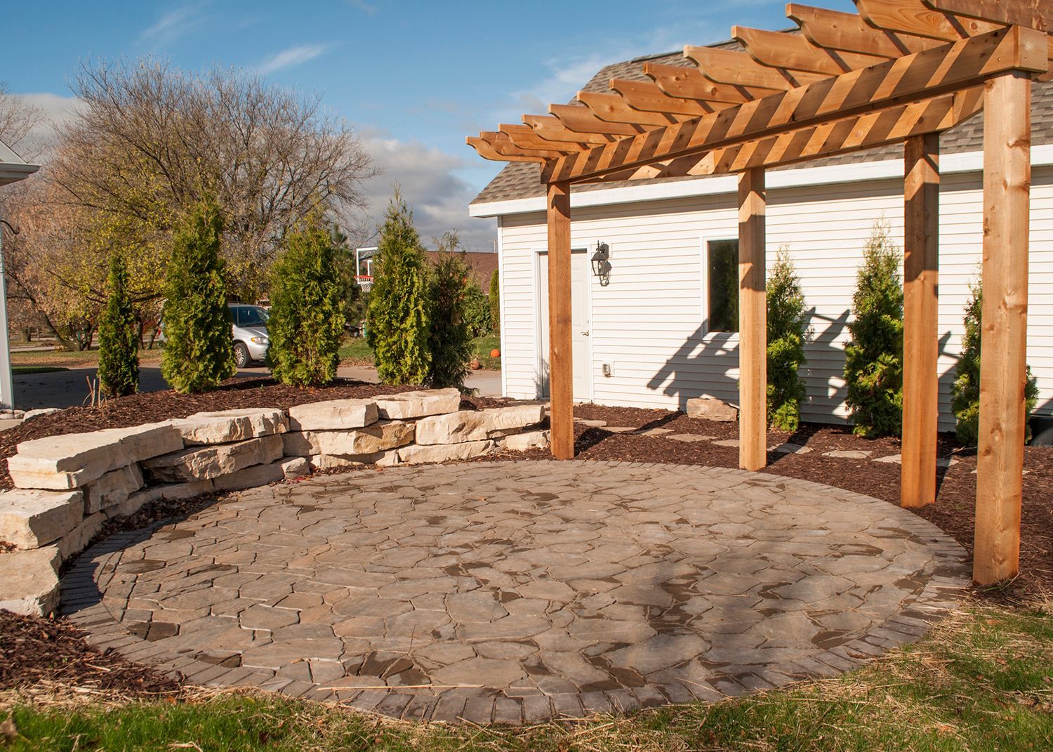 A wooden pergola is sitting in front of a white house.