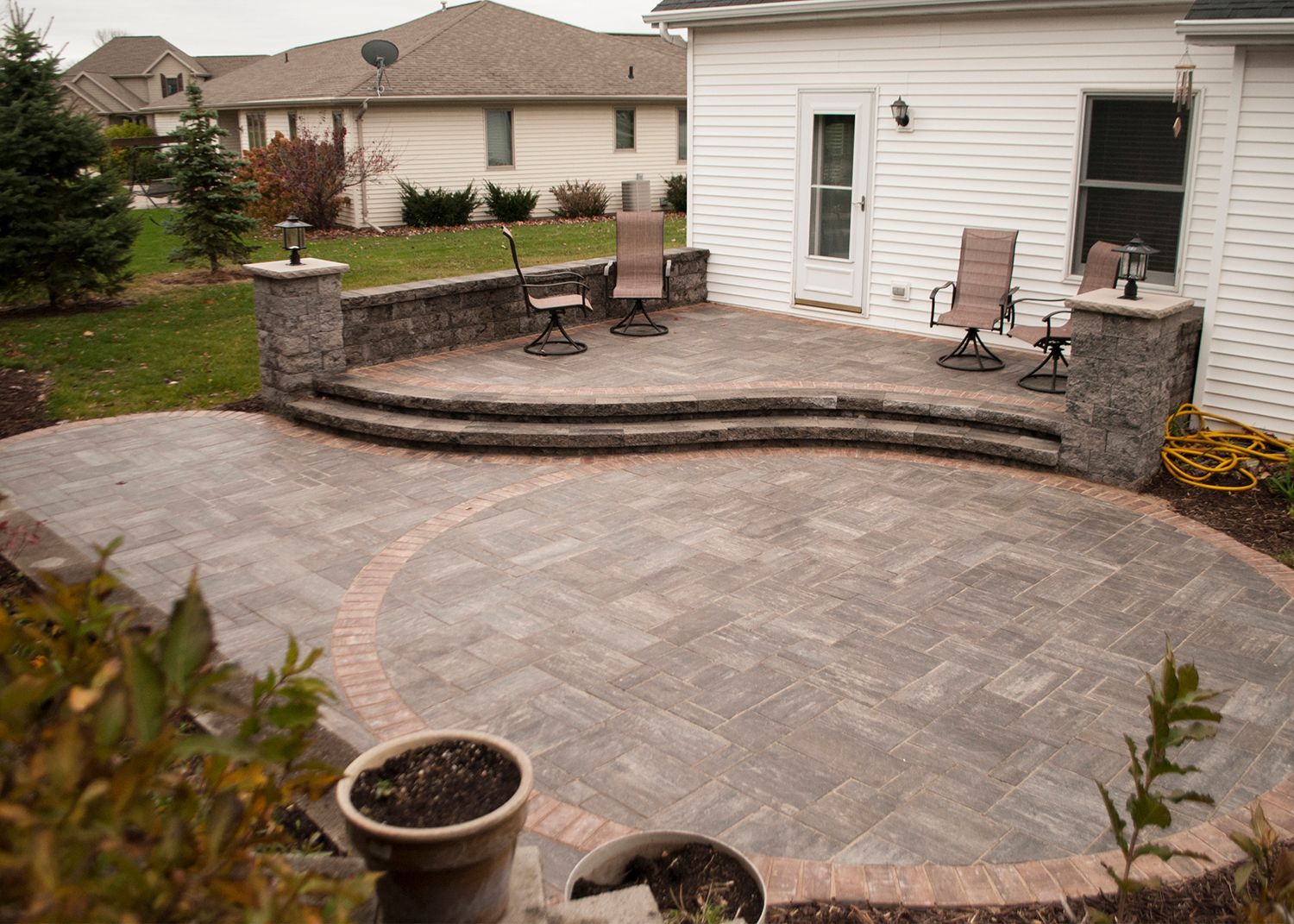 A patio with chairs and a potted plant in front of a house.