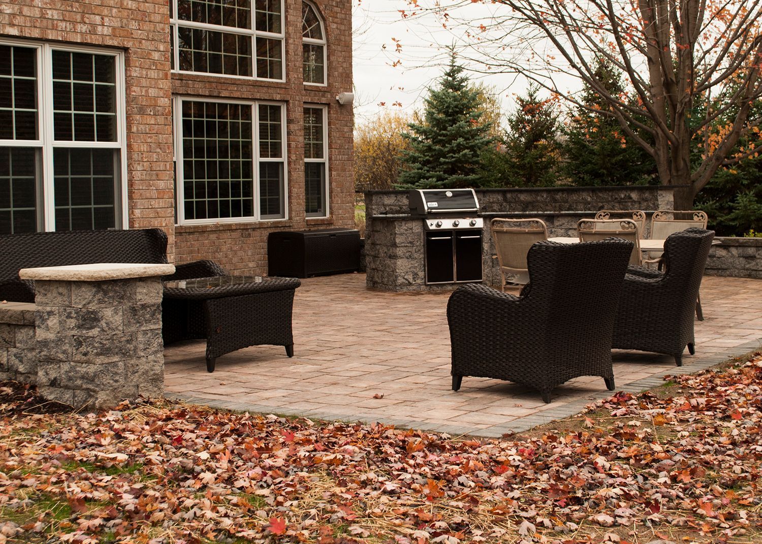 A patio with chairs and a grill in front of a brick house