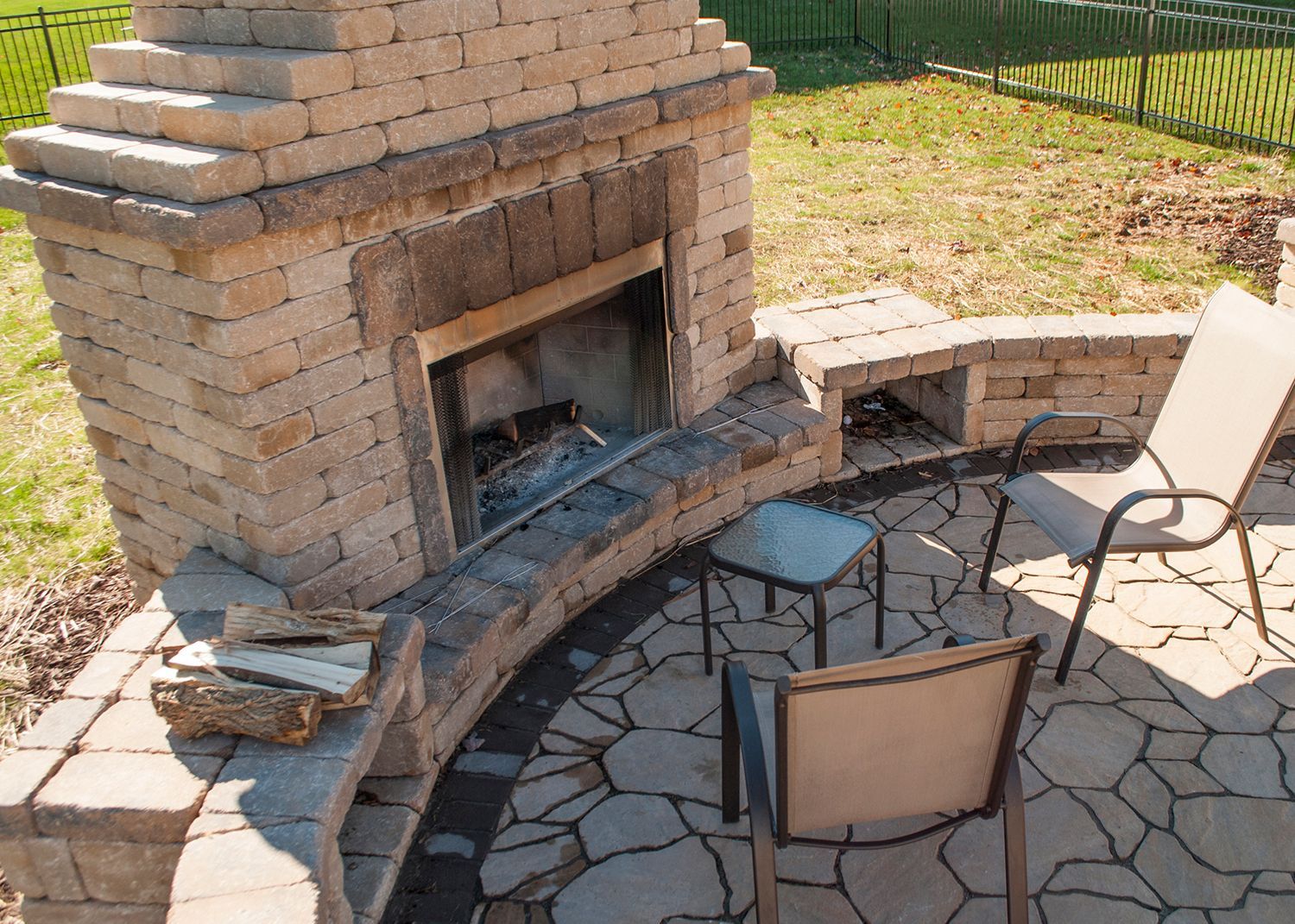 A brick fireplace on a patio with chairs and a table.