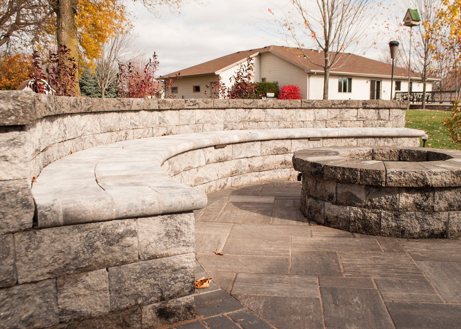 A stone wall with a bench and a fire pit in front of a house.