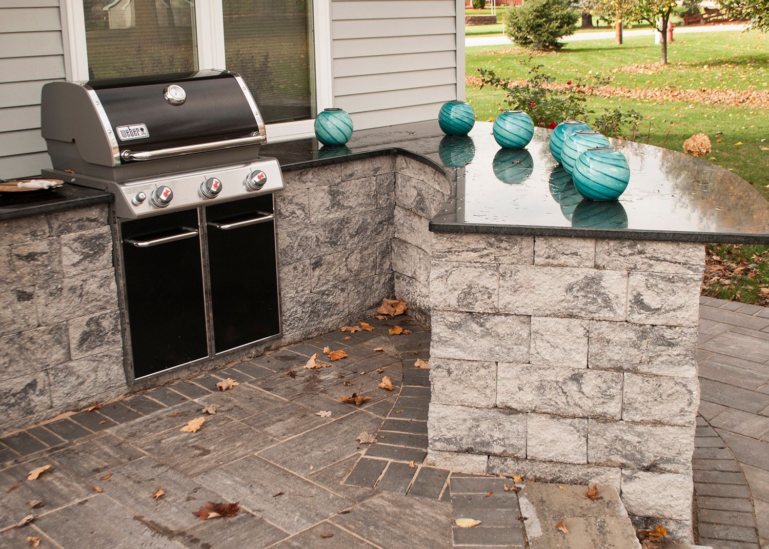 A grill is sitting on a brick patio next to a house.